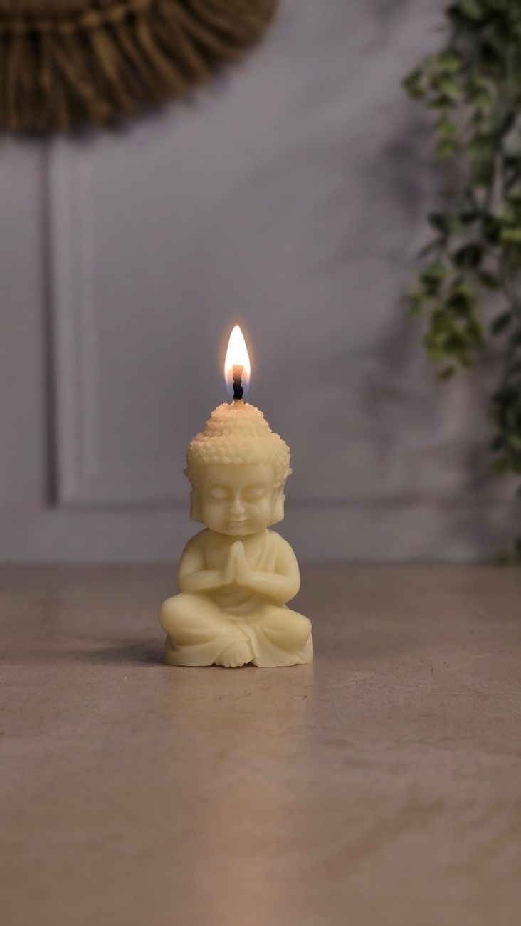 Vela de Buda encendida con los ojos cerrados, las manos en oración, sobre una superficie luminosa.