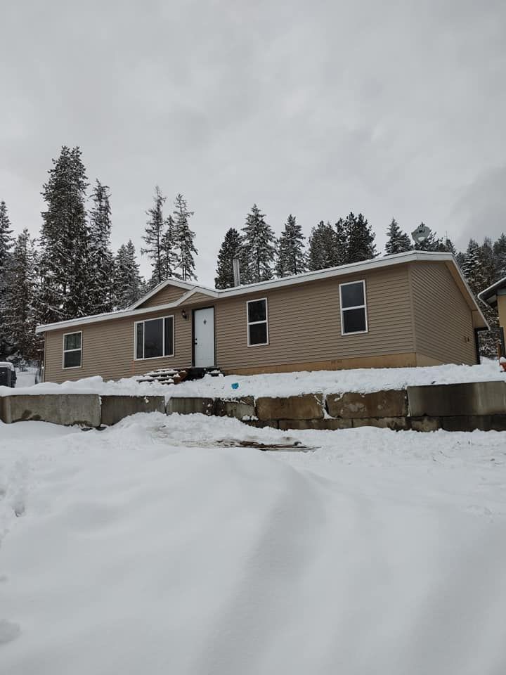 A mobile home is covered in snow and trees in the background.