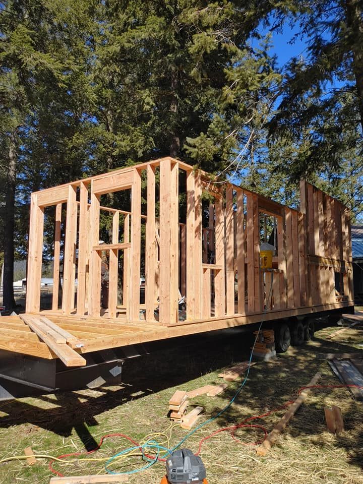 A wooden house is being built on a trailer in the woods.