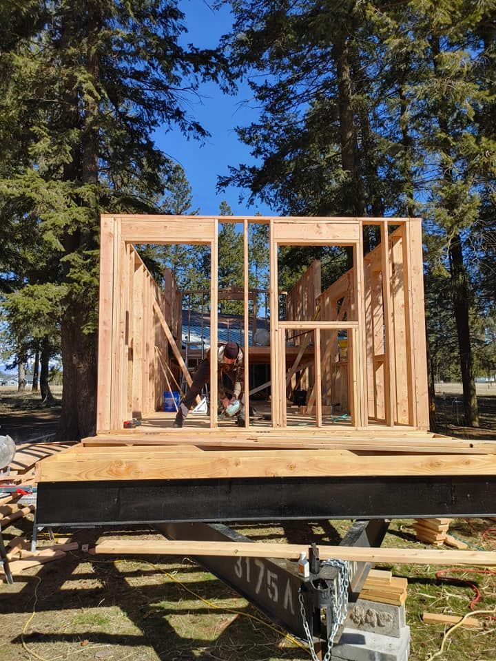 A wooden house is being built on a trailer in the woods.
