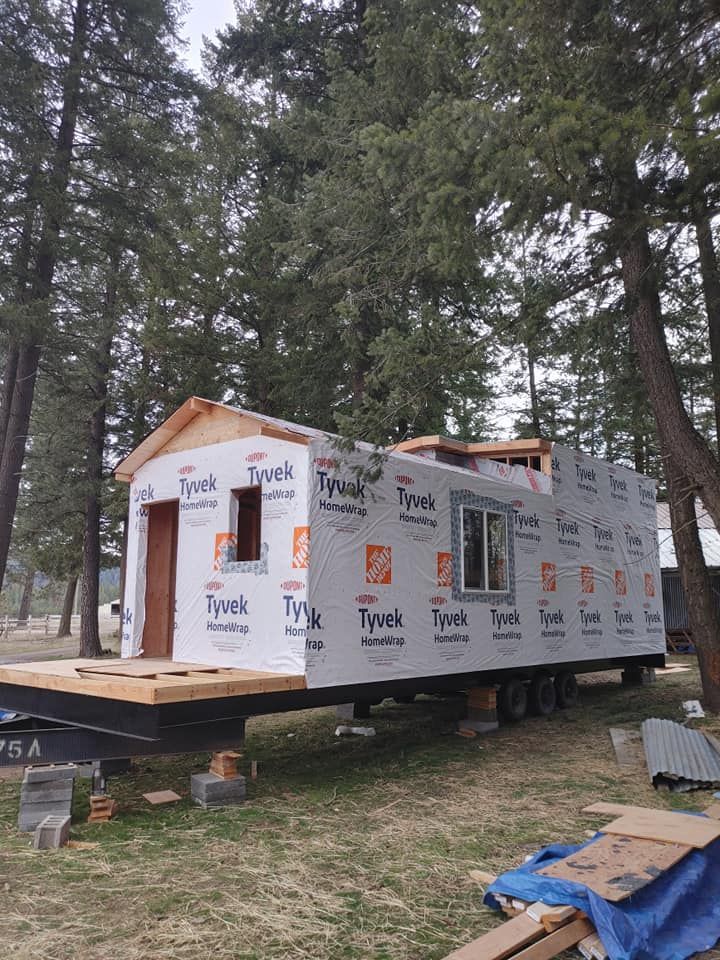 A tiny house is being built in a field with trees in the background.
