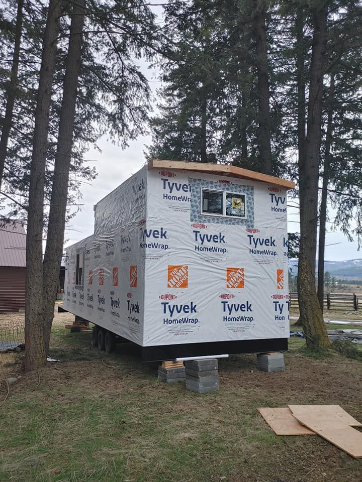 A tiny house is being built in a field surrounded by trees.