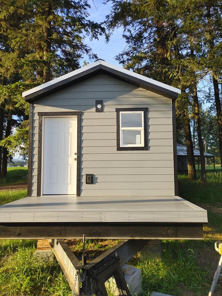 A small house is sitting on top of a trailer in the middle of a field.