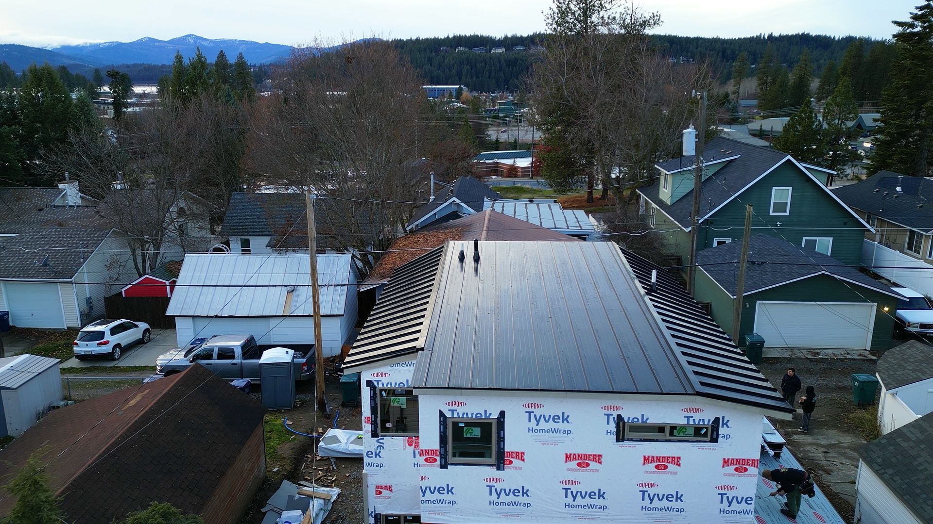 Aerial view of a house under construction with a black metal roof in a residential neighborhood.