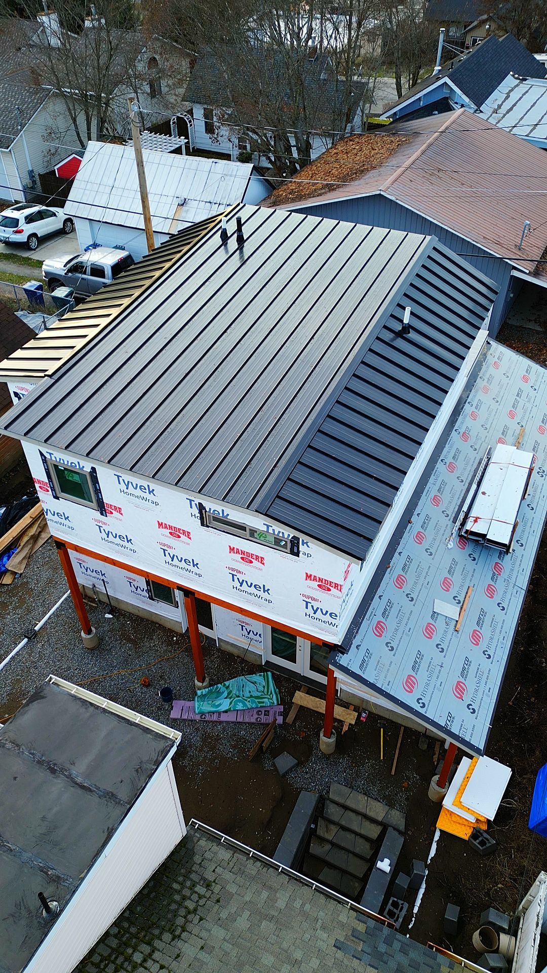 Construction site: new building with black metal roof, plywood walls, and blue tarp.