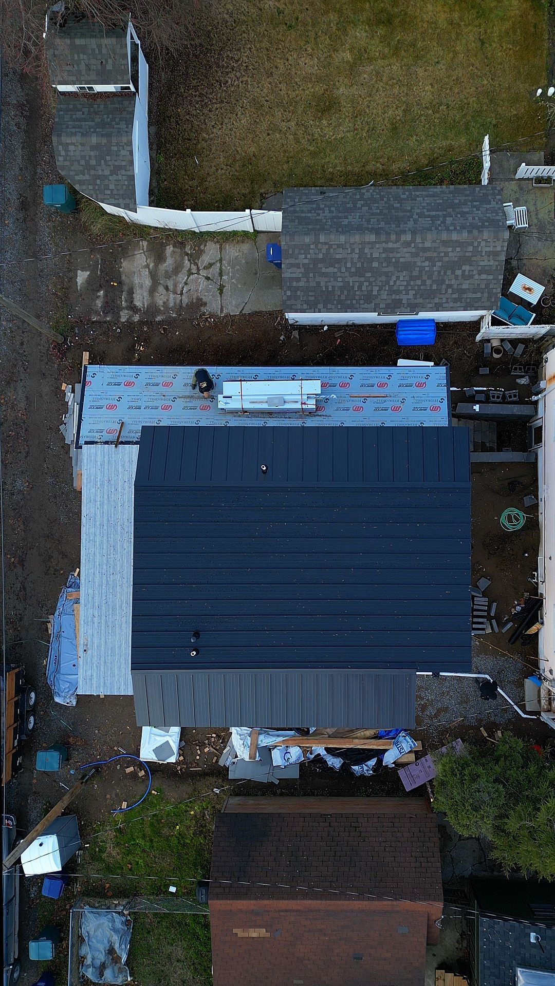 Overhead view of a house with a dark gray roof being worked on, surrounded by neighboring homes and yards.