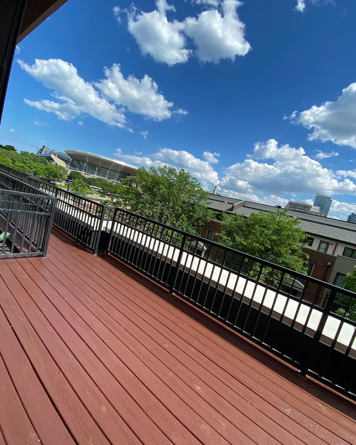 A wooden deck with a black railing and a view of a city.