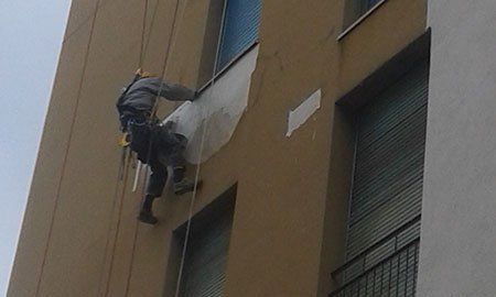 un uomo appeso a una corda al lavoro su una facciata di una casa