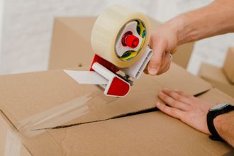 a person is using a scotch tape dispenser to seal a cardboard box