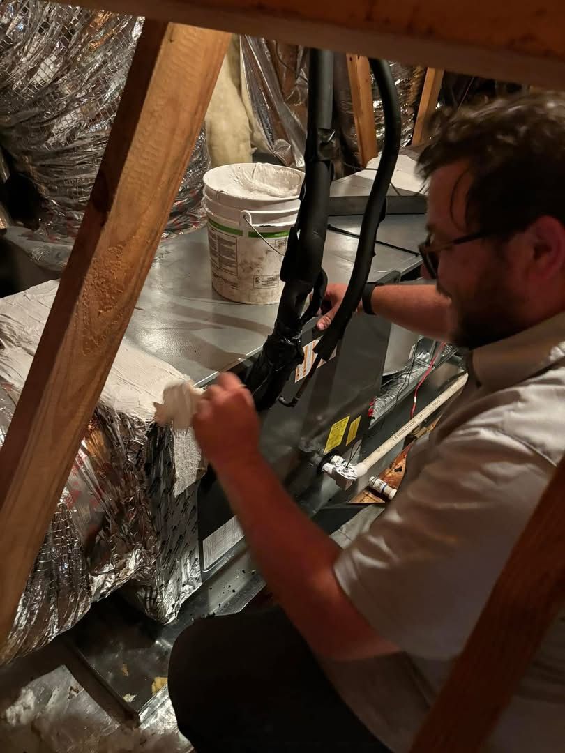 A man is working on an air conditioner in an attic.