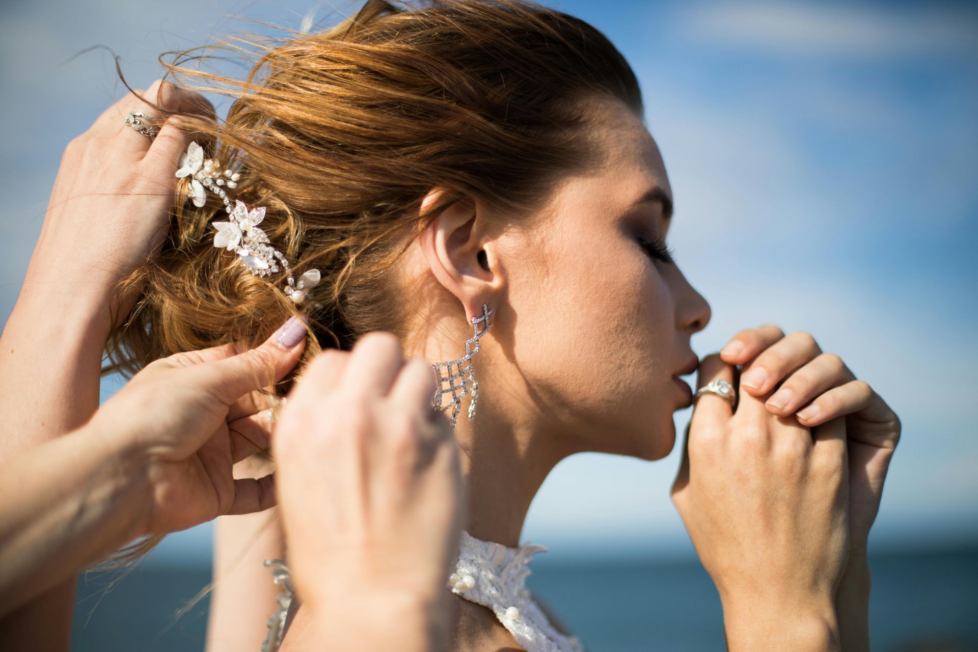 A woman in a wedding dress is getting her hair done by two women.