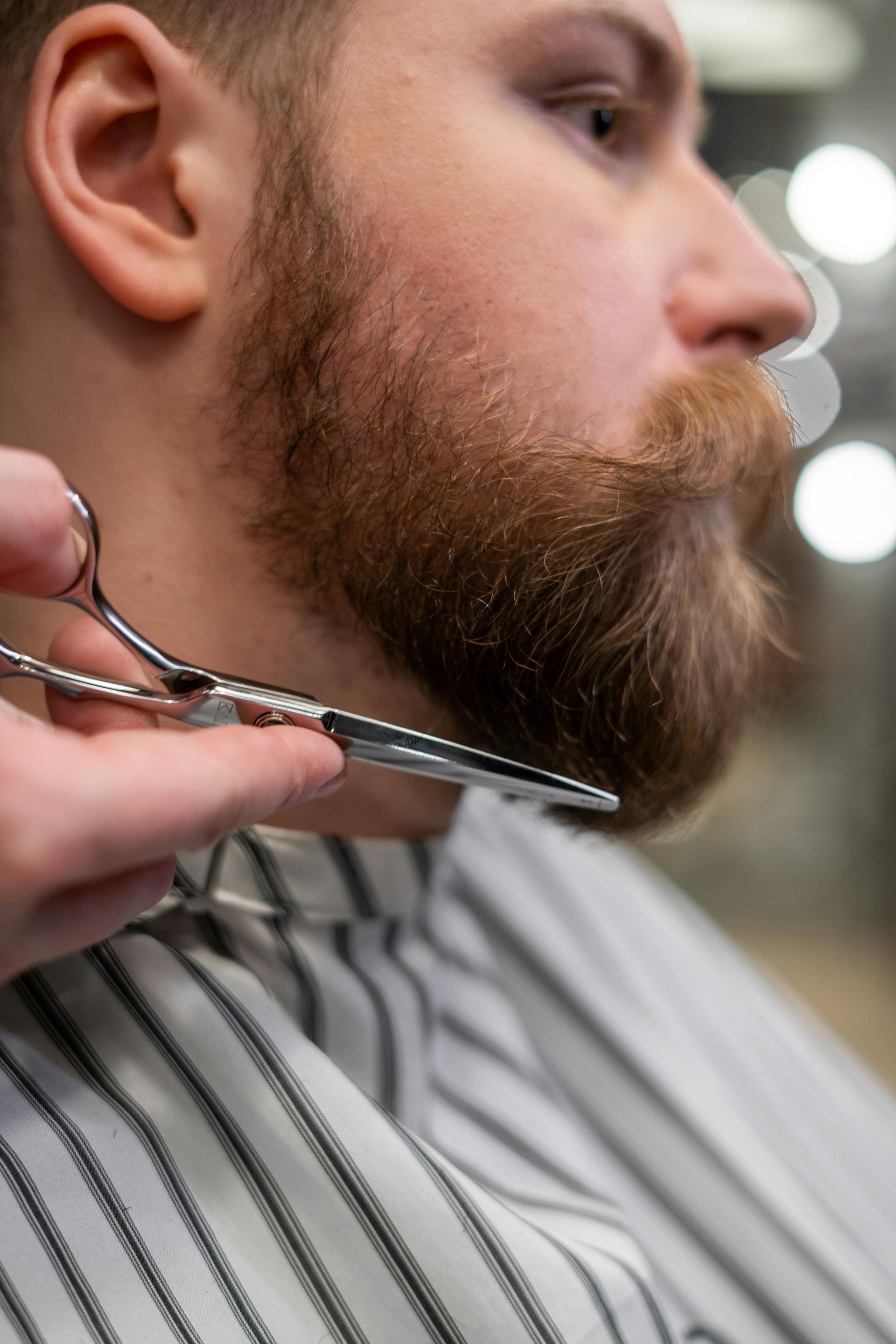 A man is getting his beard cut by a barber with scissors.