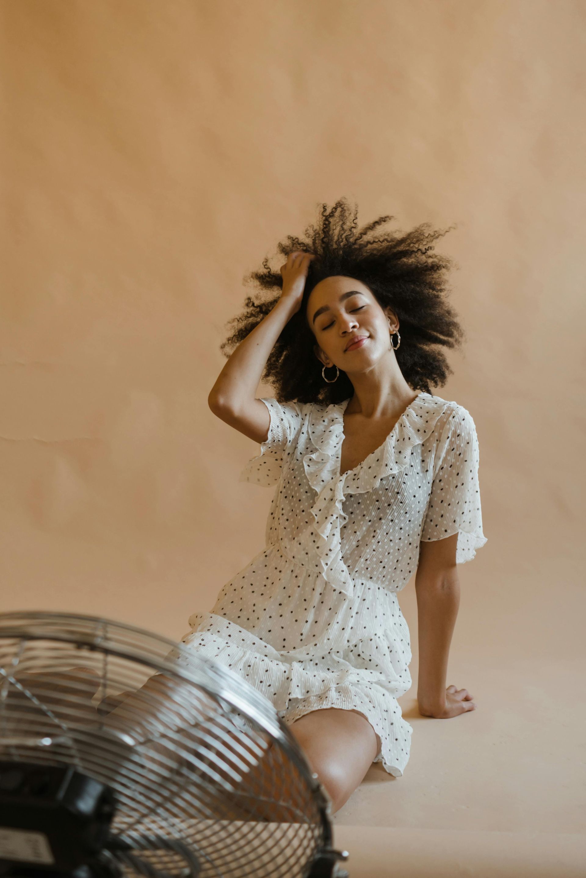 A woman in a white dress is sitting next to a fan.