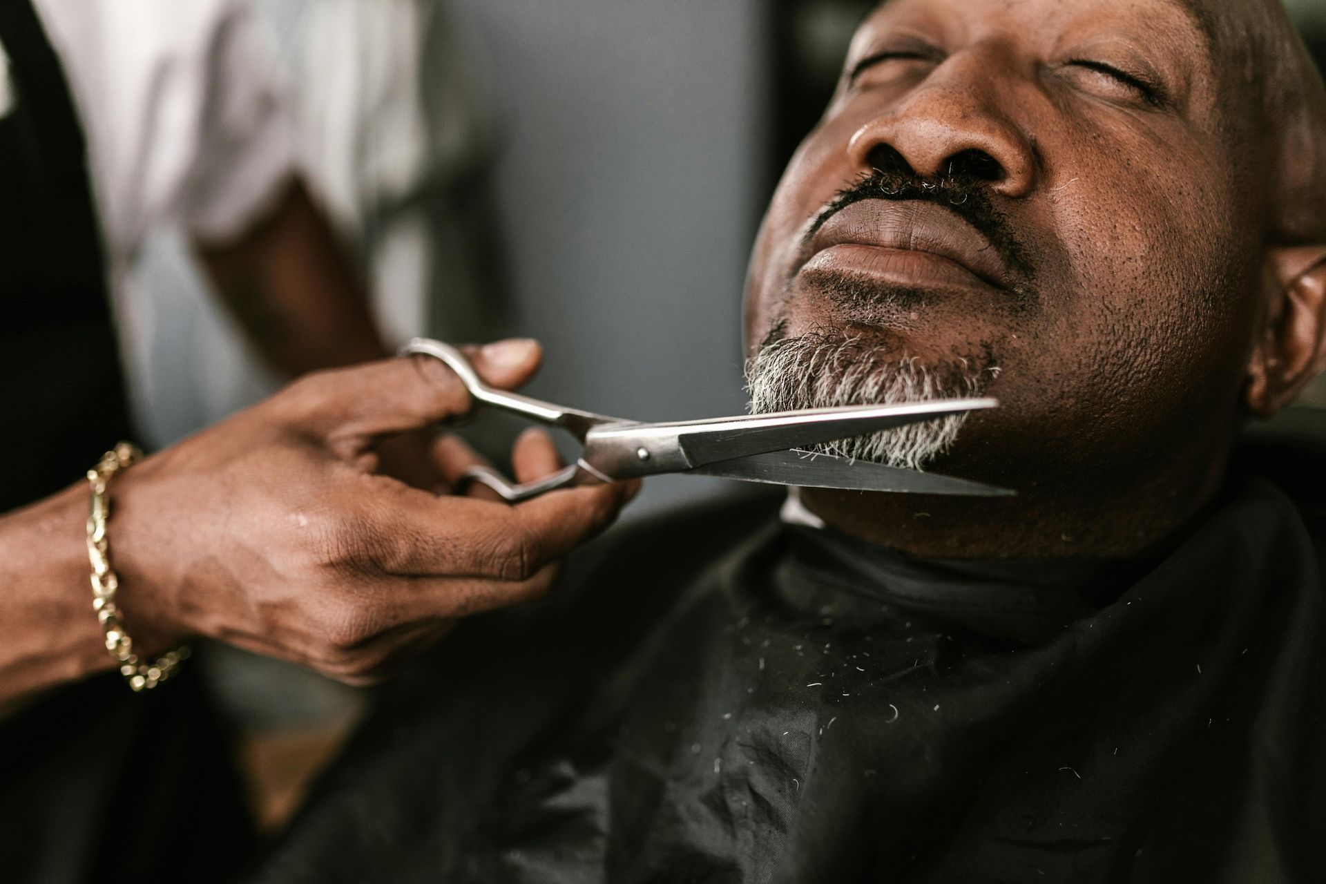 A man is getting his beard shaved by a barber with scissors.