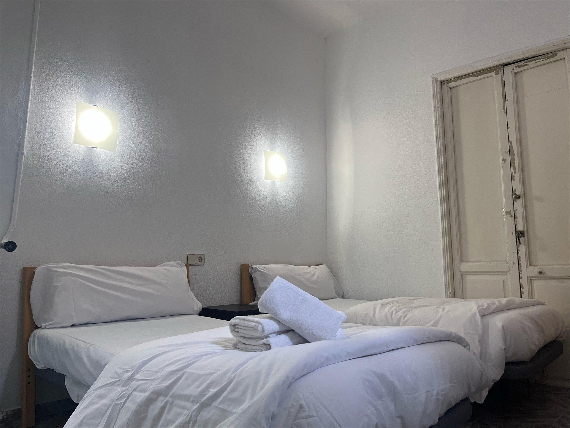 There are two beds in the room with white sheets and pillows.