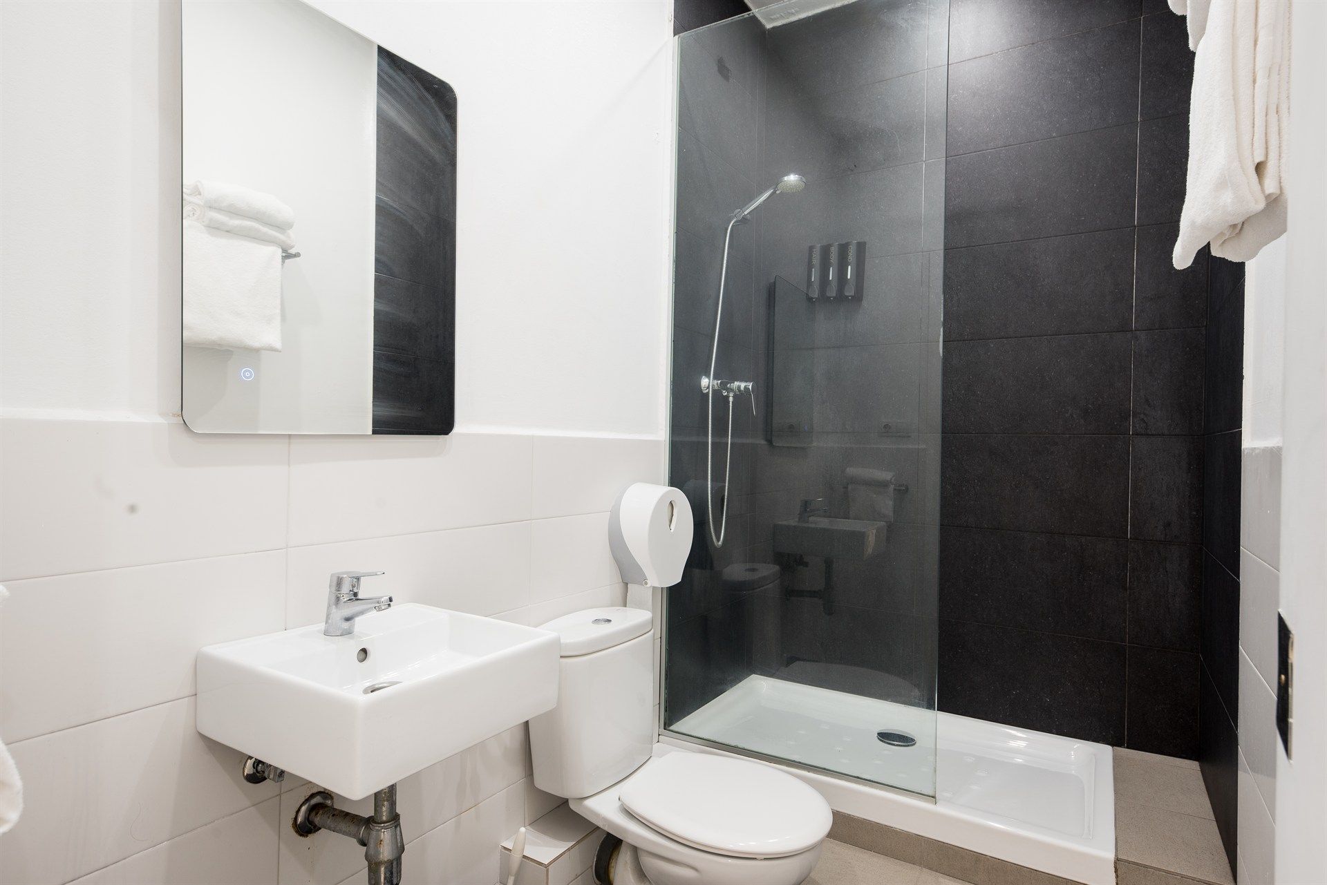 A bathroom with a toilet , sink , mirror and walk in shower.