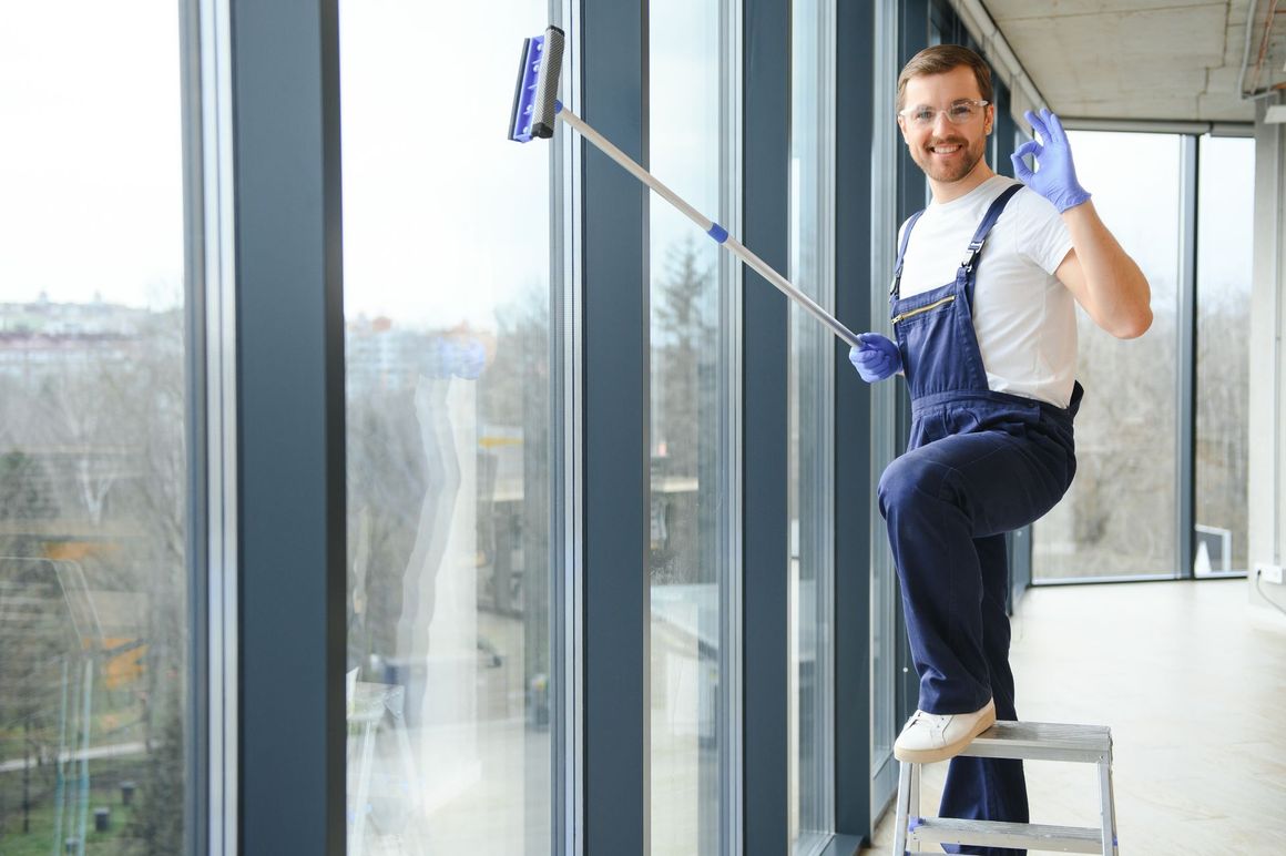 a man is sitting on a ladder cleaning a window with a mop .