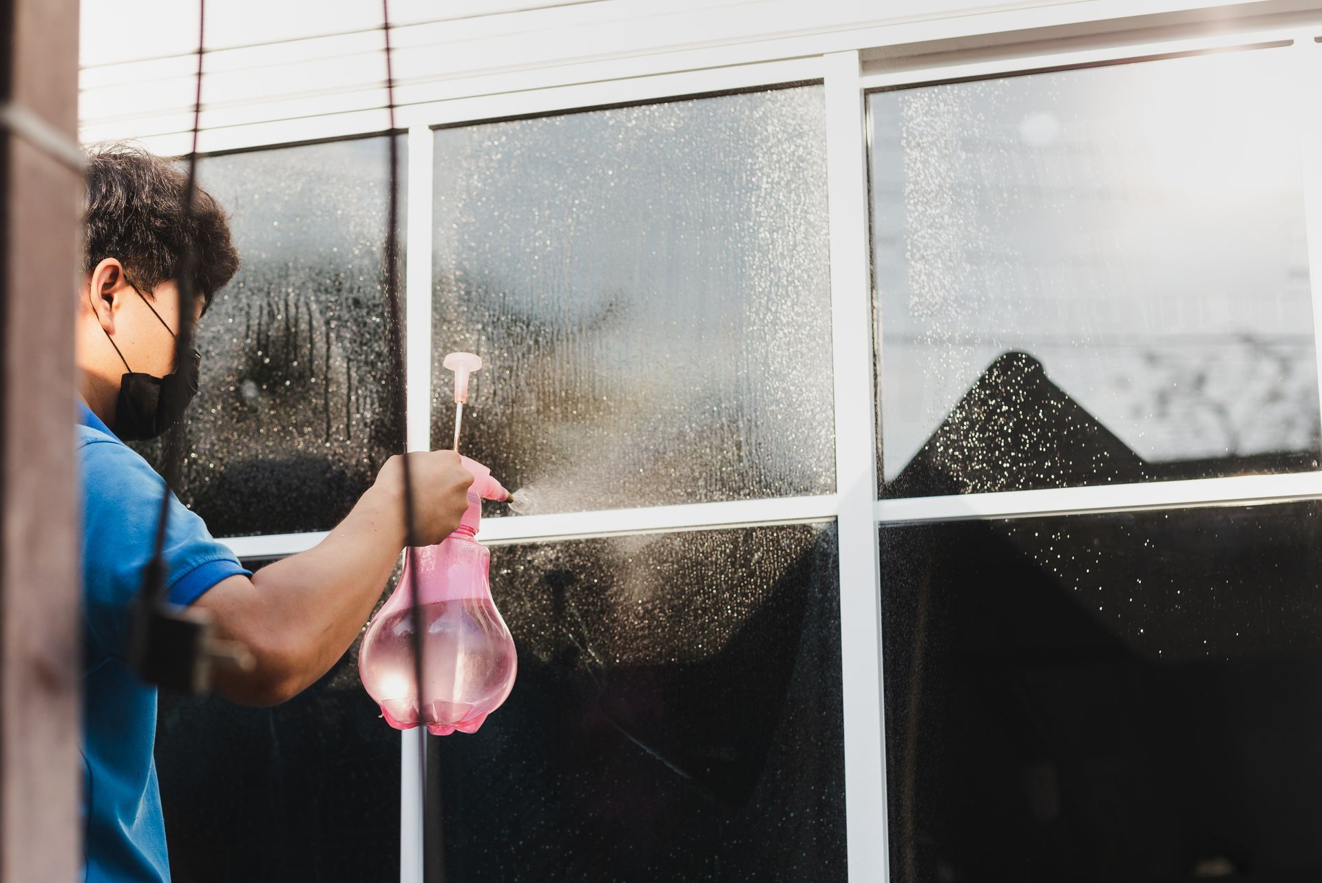 a man wearing a mask is cleaning a window with a spray bottle .