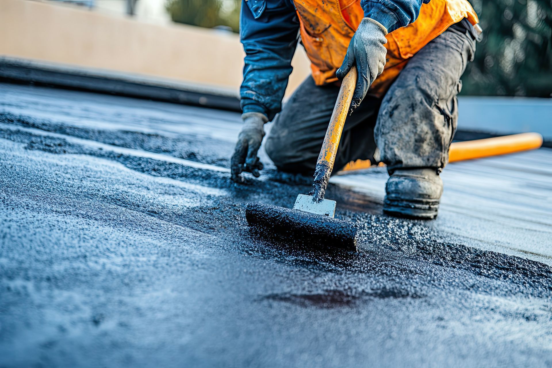 Un homme applique de l'asphalte sur un toit avec un balai.