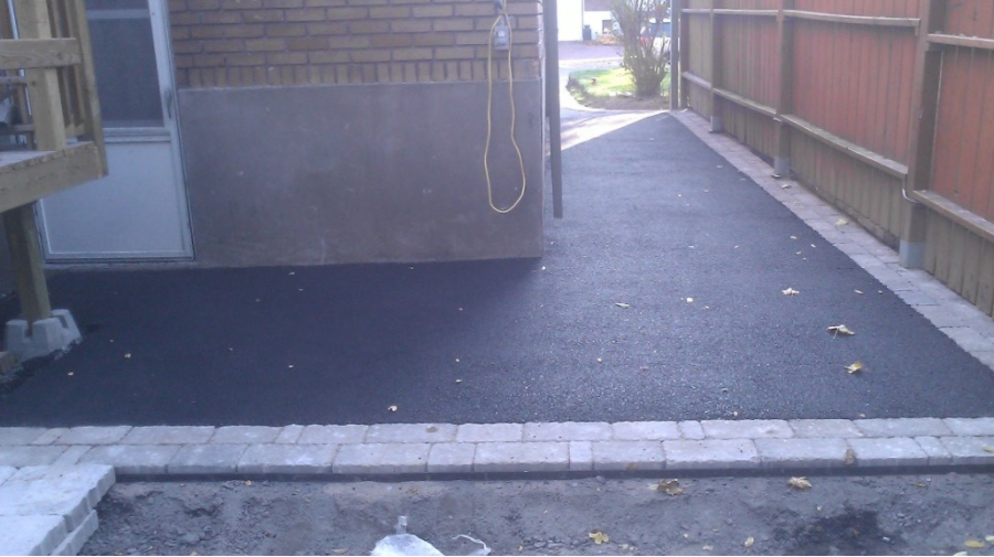 Une cour arrière avec une clôture en briques et une allée noire menant à une maison.