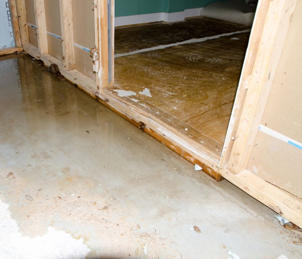 A flooded room with a wooden door and a dirty floor