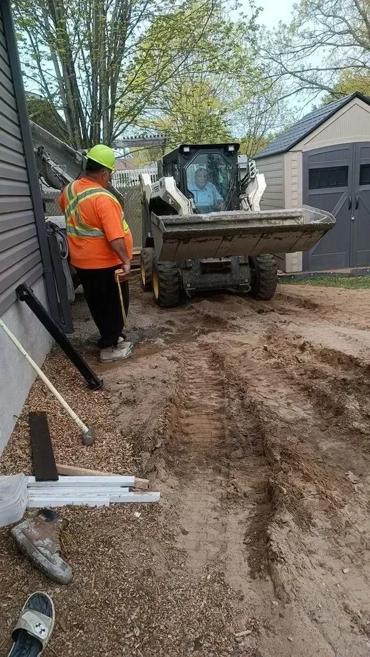 A man is standing next to a bulldozer moving dirt in a driveway.