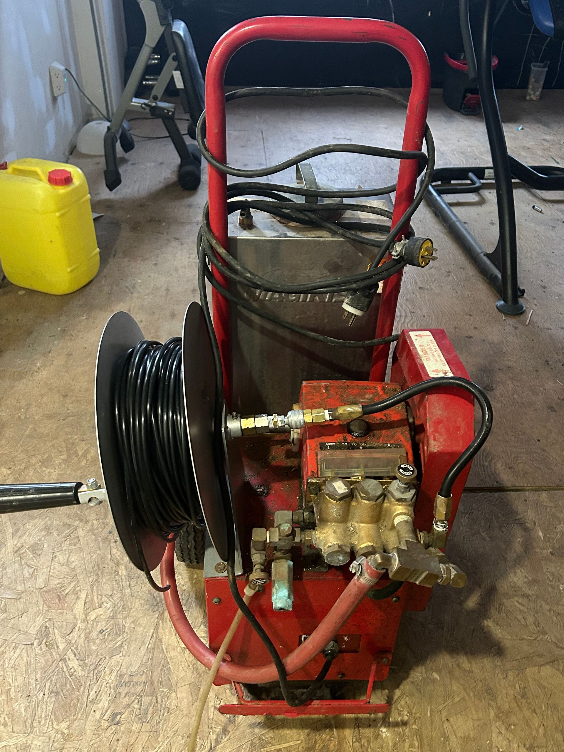 A red pressure washer with a hose attached to it is sitting on a wooden floor.