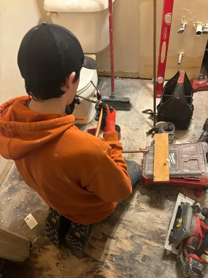 A young man is kneeling on the floor in a bathroom working on a toilet.