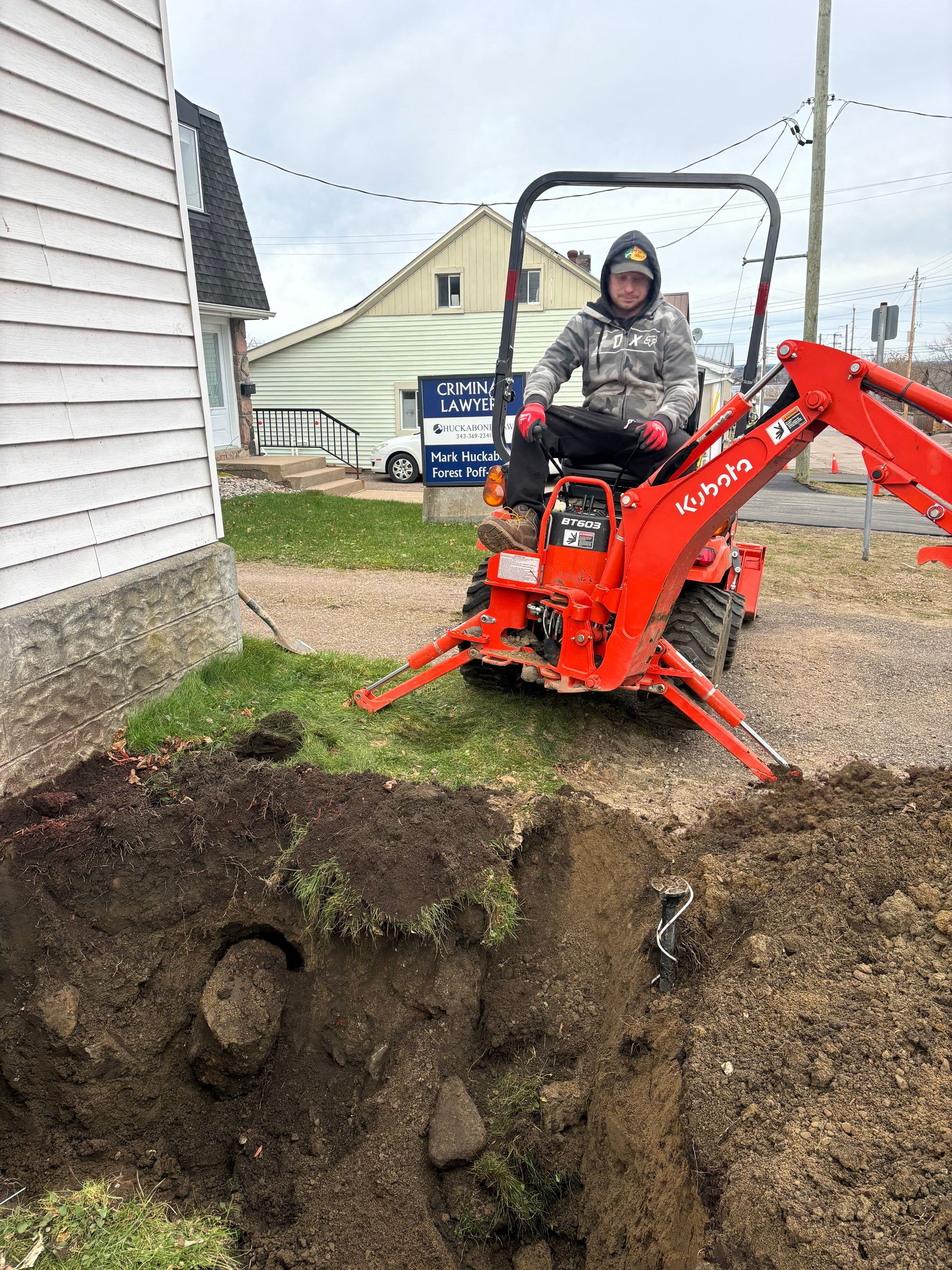 A man is driving a small red excavator in a hole in the ground.