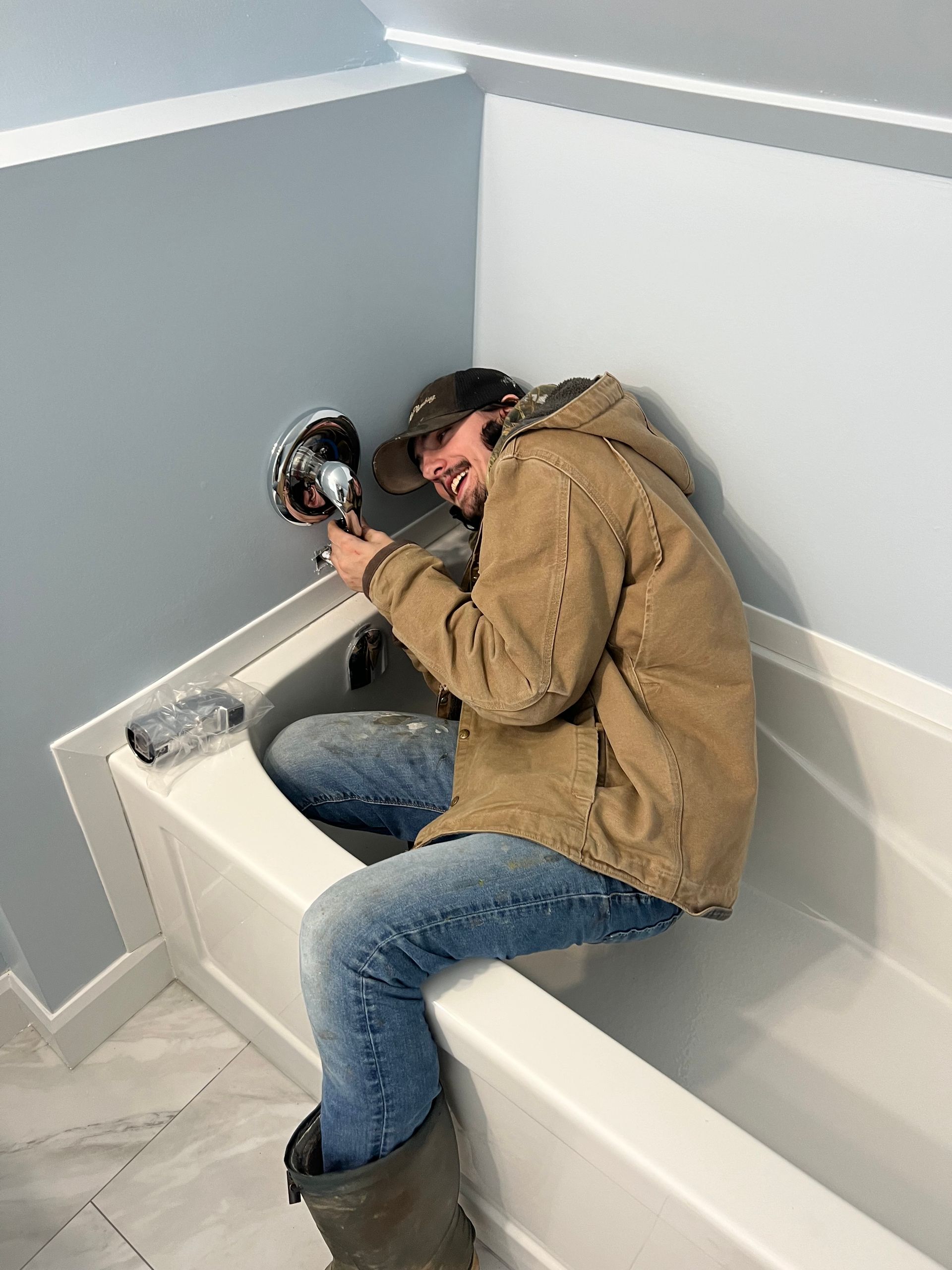 A man is sitting on the edge of a bathtub holding a tool.