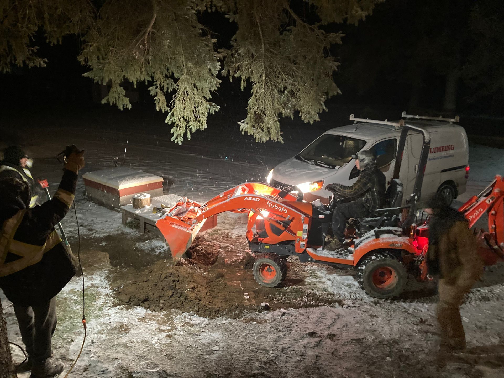 A man is standing next to a tractor in the snow at night.