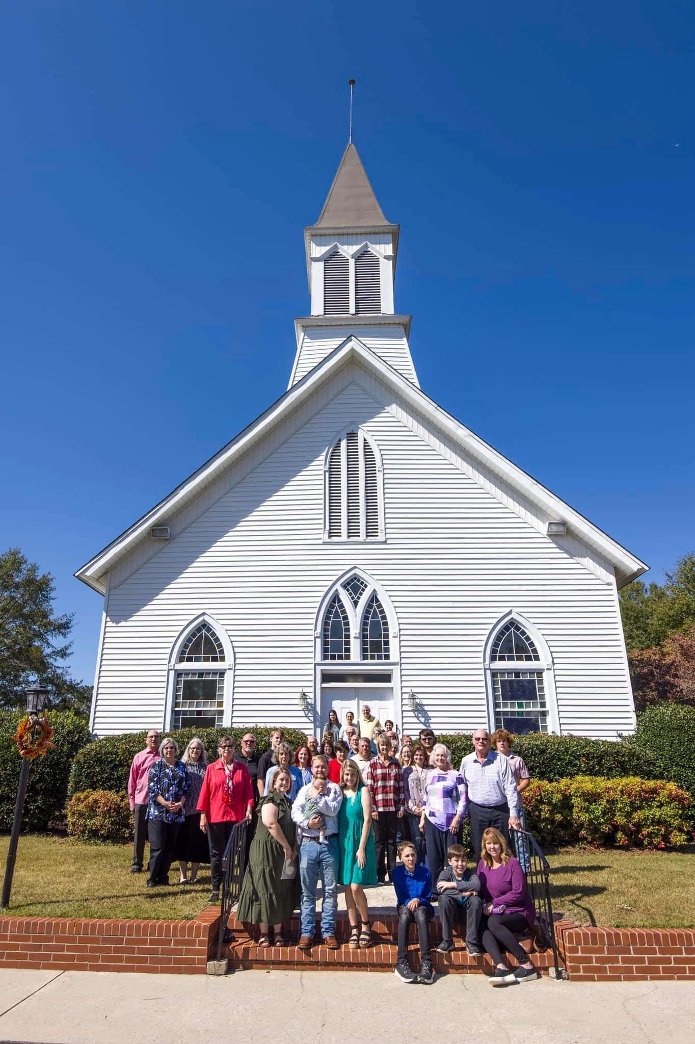 A group of people are posing for a picture in front of a white church.