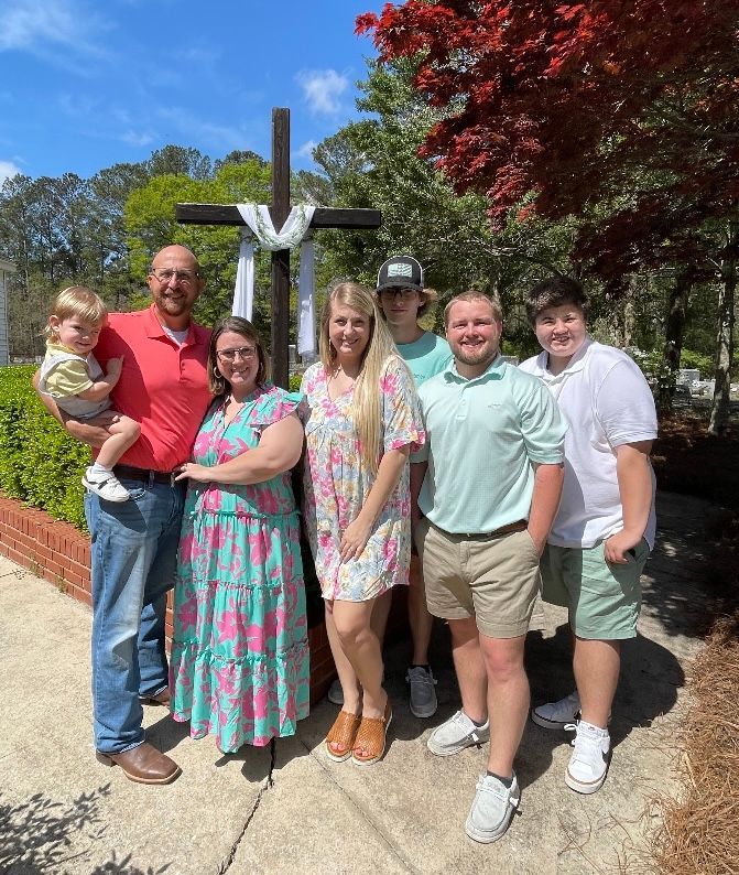 A family is posing for a picture in front of a cross.