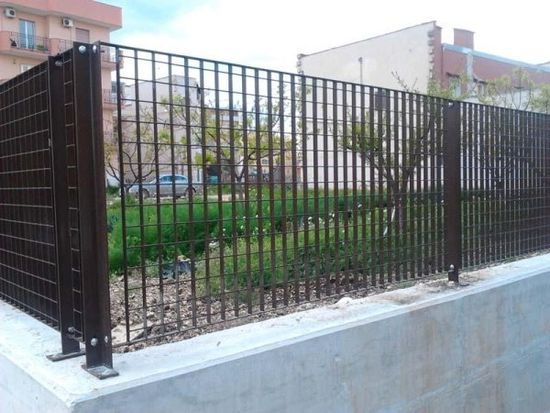 Una recinzione metallica circonda un muro di cemento in un parco.
