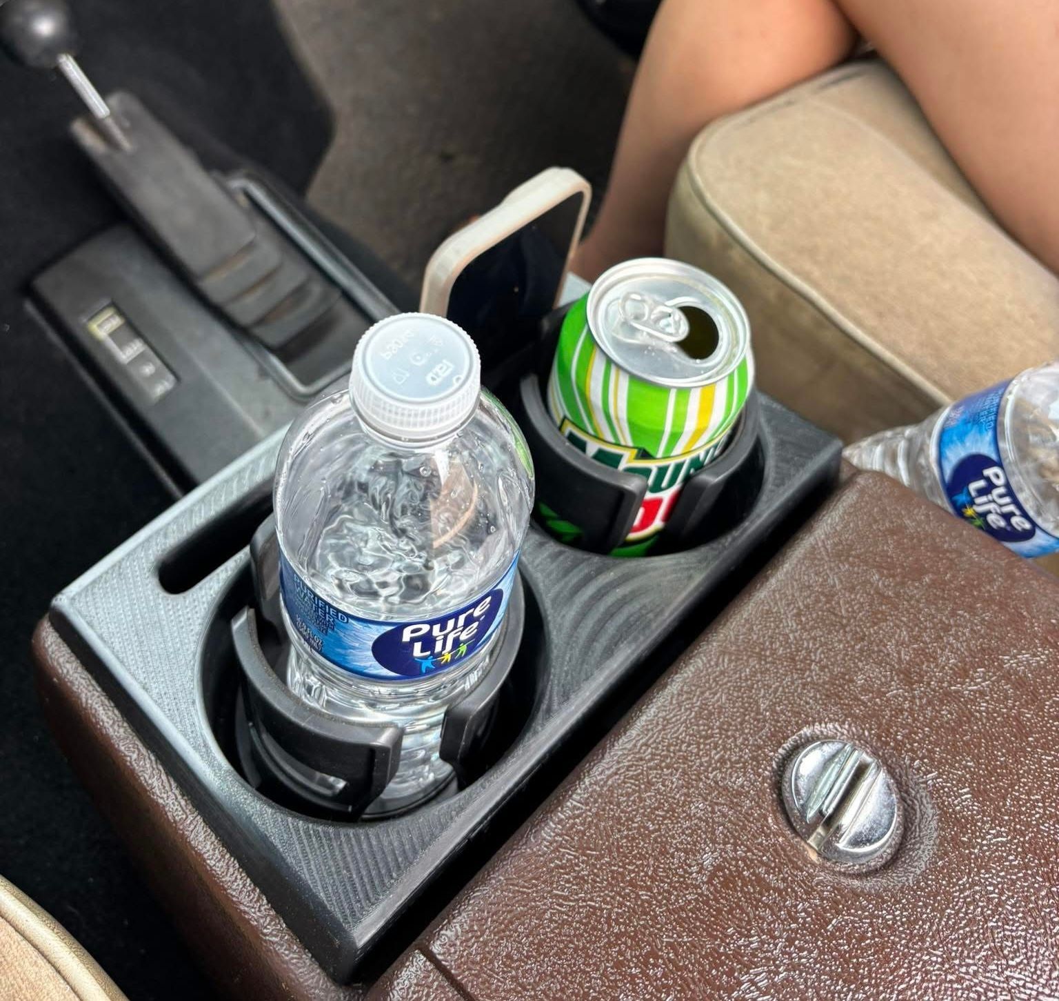 Brown car console with 3D printed cup holder holding water bottle, soda can, and phone.