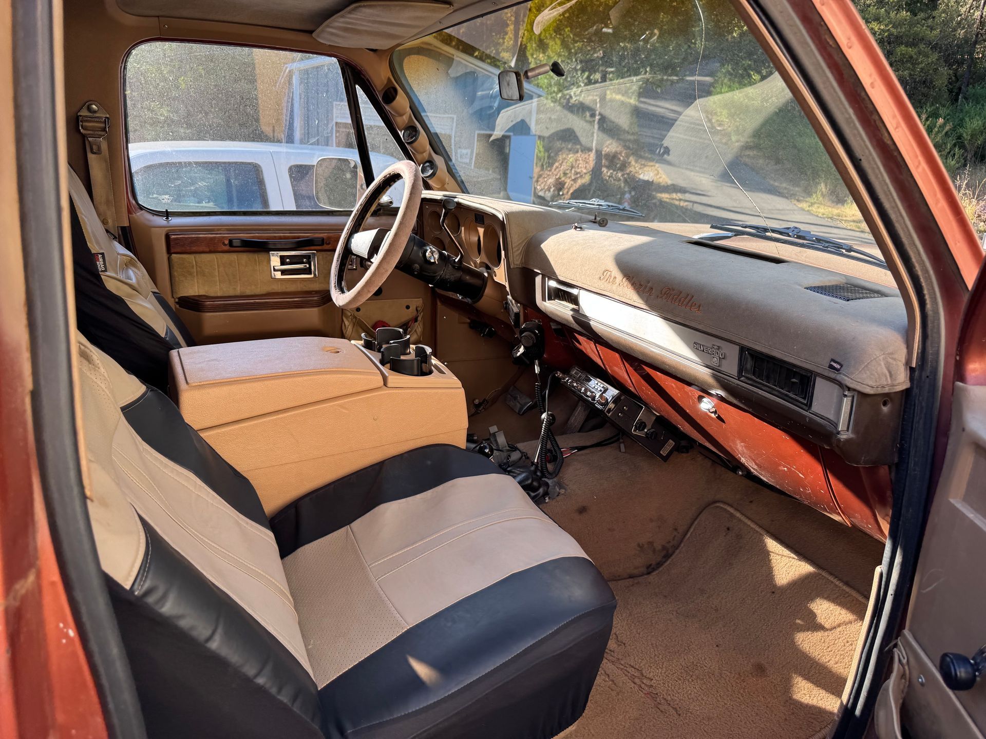 Interior of a vehicle, focused on gear shift and steering wheel. Beige carpet, black and silver details, neutral tones.