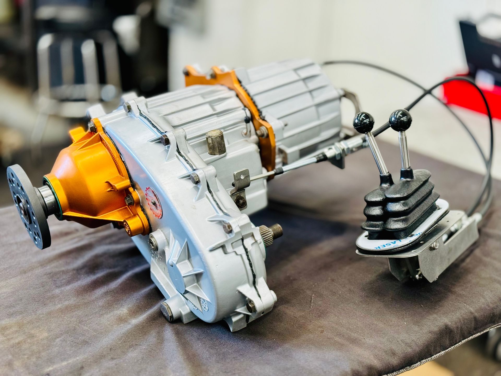 Silver transfer case with black shift levers and a shift boot, on a work surface.