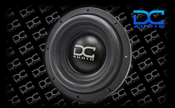 Black DC Audio subwoofer with a rubber surround against a dark background with the DC Audio logo.