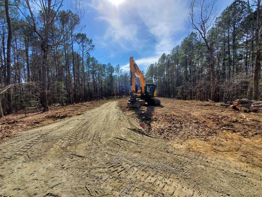 a yellow excavator is driving down a dirt road in the middle of a forest .