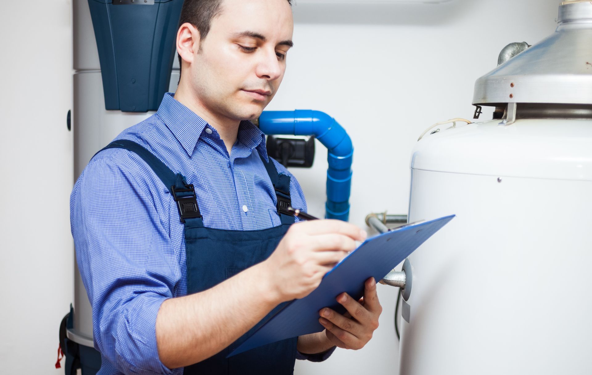 Plumber inspecting residential water heater and taking notes during routine maintenance check.