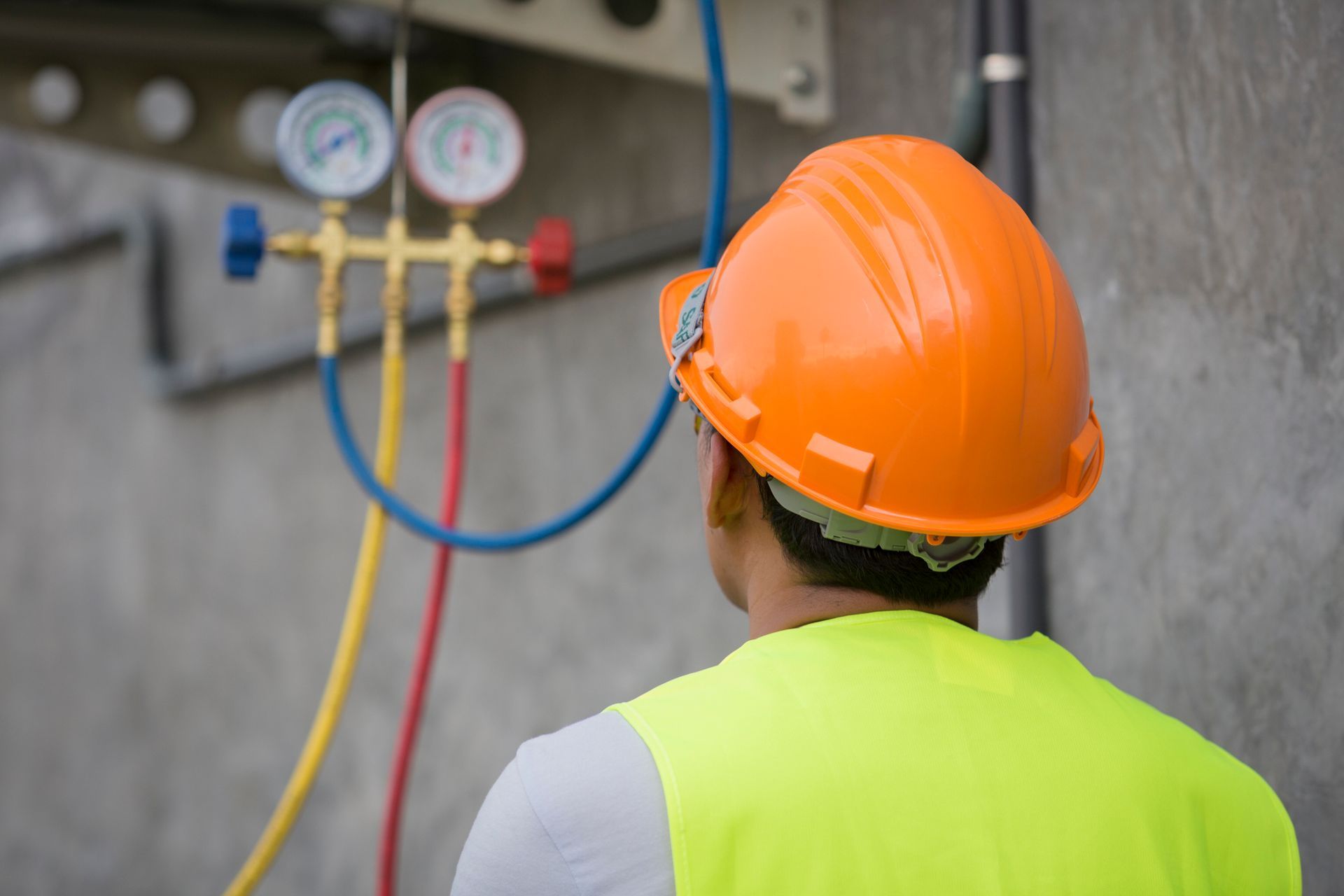 Worker in safety gear checking pressure gauges on a wall.