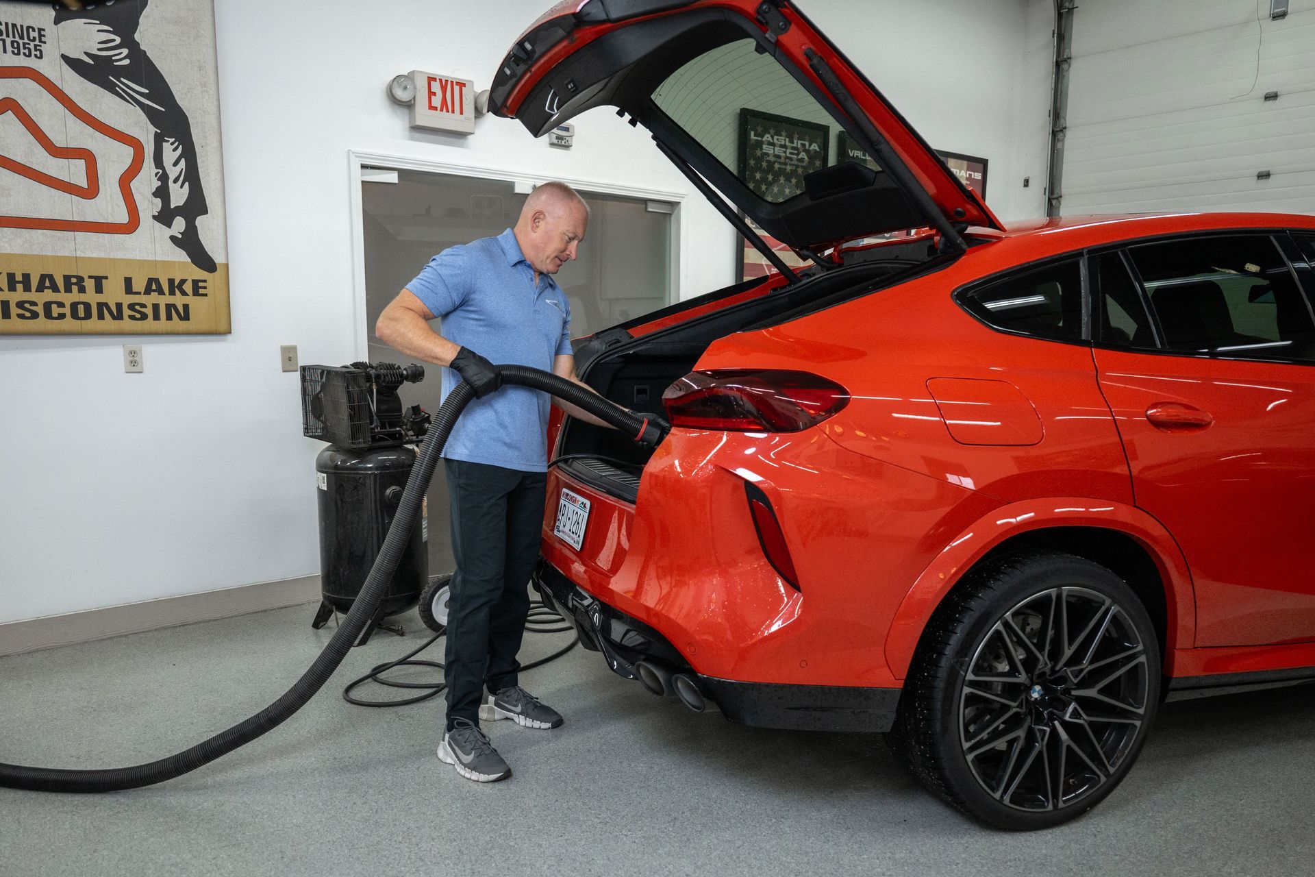 Man vacuuming the trunk of a bright orange car inside a garage.