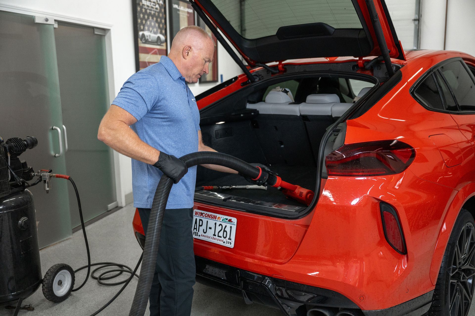 A man vacuums the trunk of a red car in a garage.