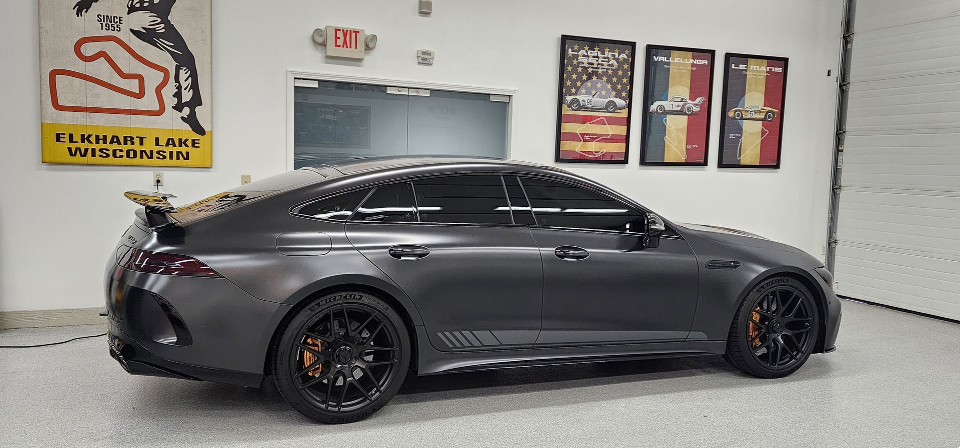Dark gray Mercedes-AMG GT 4-Door Coupe parked in a garage, with black wheels and orange brake calipers.