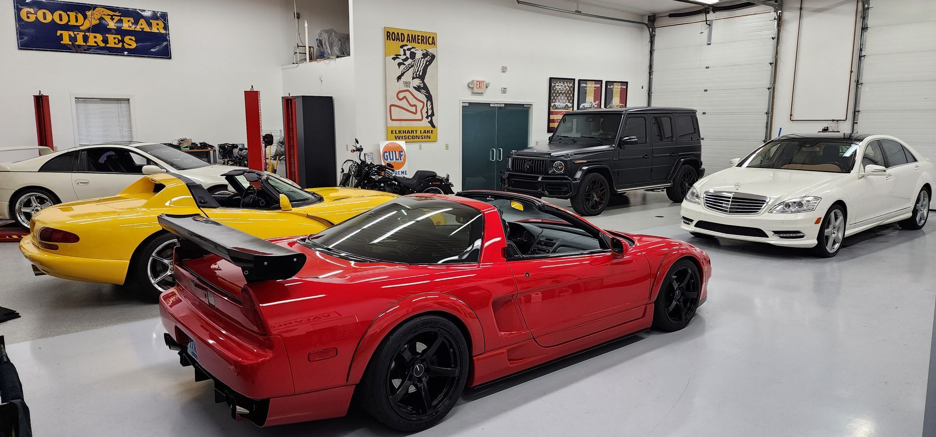 A red sports car in a garage with other cars, including a yellow sports car, a black SUV, and a white sedan.