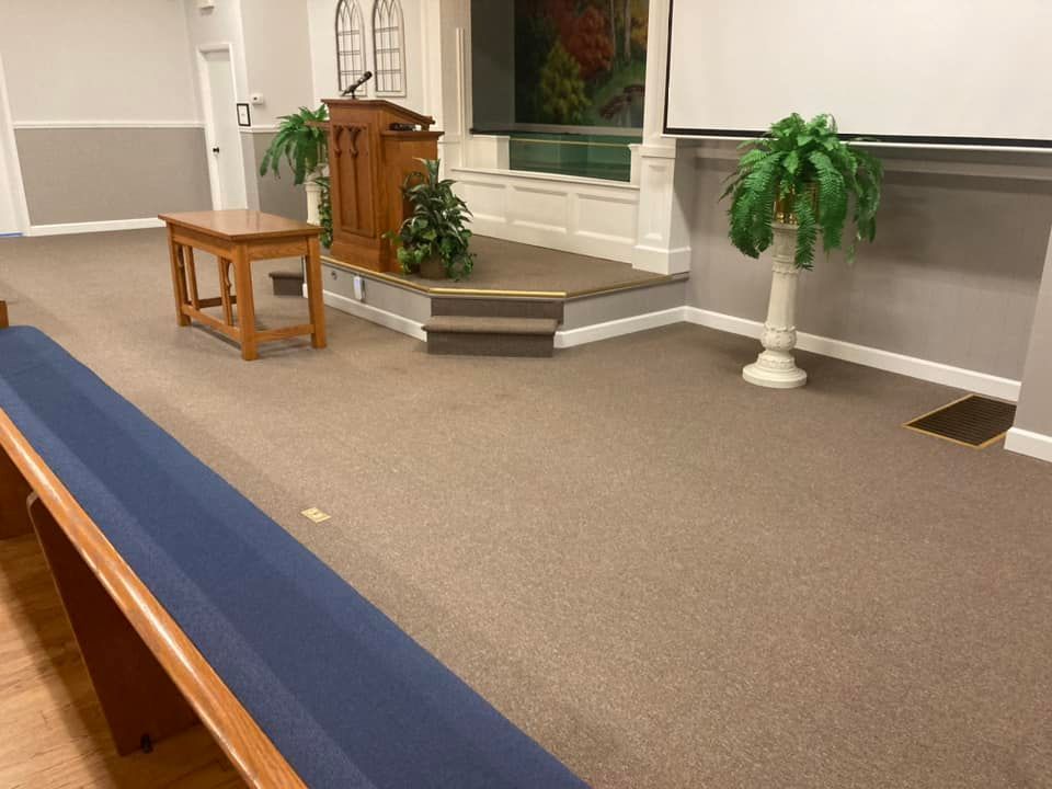 A church sanctuary with a wooden pulpit and altar on a raised platform, empty pews.