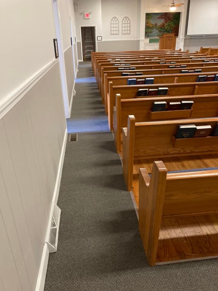 Empty church auditorium with rows of wooden pews, a wall with wainscoting, and a center aisle.