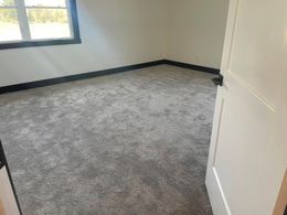 Empty room with gray carpet and white door, black trim.