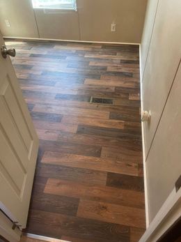 Open doorway into a room with brown, wood-look flooring.