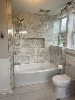 Bathroom with marble tile, gold fixtures, tub, toilet, and window.